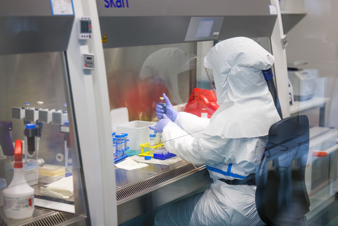 Forscher*in in Schutzanzug untersucht Tuberkulose Stämme in einem Labor.