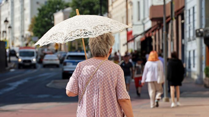 An elderly woman walks in the summer heat with a parasol.
